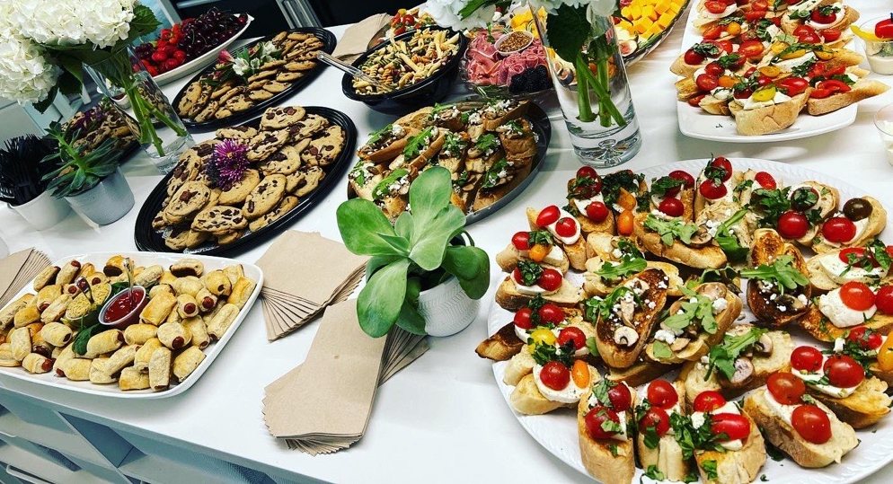 An MBB catering spread — cookies, bruschetta on baguette, pigs-in-a-blanket, charcuterie