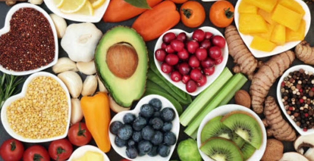 Fresh produce and superfoods in white heart-shaped bowls — berries, avocado, ginger, kiwi, peppers